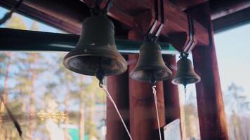 schließen oben von drei Glocken auf das Hintergrund von verschwommen Blau Himmel und Bäume. . Eisen Glocken hängen im ein hölzern Bogen. video