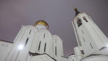 bas vue de une gros blanc église avec d'or dômes et une cloche la tour. action. orthodoxe église sur foncé nuit ciel Contexte en dessous de rue les lampes. video