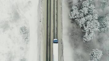 aereo Visualizza di traffico su il strada passaggio attraverso il inverno foresta nel acuto tempo atmosferico. scena. superiore Visualizza di un' carico camion in movimento su un' dritto strada circondato di neve coperto boschi. video