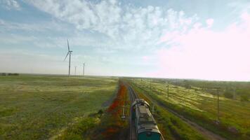 Top view of summer landscape with moving train. Shot. Drone flies with moving train on background of green fields. Train rides on railway in green field on background of horizon on sunny day video