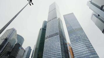 Bottom view of high rise buildings with glass windows and the cloudy foggy sky. Action. Beautiful modern skyscrapers in a city business district. video