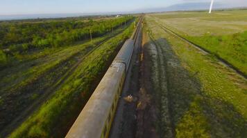 Top view of freight train on green field background. Shot. Drone follows train at speed. Train rides with load on railway on background of green field on sunny day video