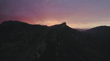 topp se av berg på bakgrund av lila solnedgång himmel. handling. mörk silhuetter av bergen på bakgrund solnedgång himmel. dyster himmel över mörk toppar av bergen video