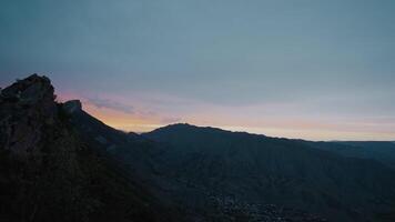 puesta de sol terminado oscuro montaña valle. acción. crepúsculo en oscuro montaña valle. panorama de pequeño montaña Valle con pueblo en antecedentes de puesta de sol video