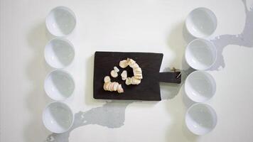 superiore Visualizza di un' bianca tavolo, bianca ciotole e un' nero di legno asse, cucinando asiatico piatto. . taglio ingredienti e mettendo loro in il ciotole separatamente con un' fermare movimento effetto. video