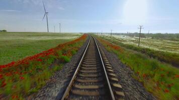 oben Aussicht von schön Eisenbahn auf Hintergrund von Grün Feld. Schuss. Wind Bauernhof in der Nähe von schön Eisenbahn im Grün Feld. malerisch Eisenbahn mit rot Blumen im Grün Feld mit Windmühlen video