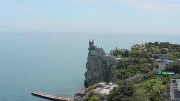 Top view of castle on edge of steep cliff. Action. Beautiful white castle is located above rocky cliff near blue sea. Swallow's Nest castle on shore in Crimea video