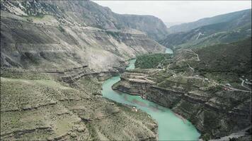 aéreo ver de un curva verde río fluido entre rock laderas acción. verano natural paisaje con un pintoresco corriente y montaña rango. video