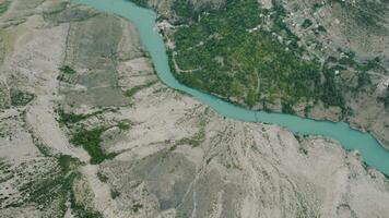 Top view of turquoise river in mountain valley. Action. Beautiful turquoise river on flat valley near rocky mountains. Turquoise mountain river near rocky reliefs video