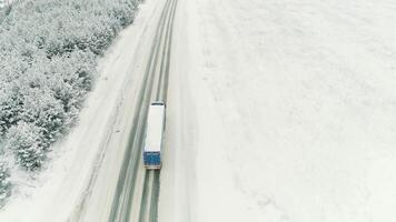 Aerial view of a logging truck driving on an empty road leading through snowy spruce forest. Scene. Concept of transportation, a truck moving along snow covered winter nature. video