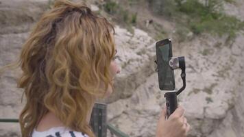 Beautiful woman takes pictures on phone with steadicam. Action. Young woman takes pictures on phone with manual stabilizer. Traveler takes pictures on hand-held steadicam in mountains video