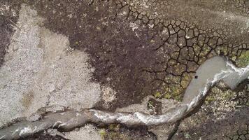 Aerial top view of a bending narrow stream flowing along rare growing grass and soil. Shot. Dry ground and curving stream. video