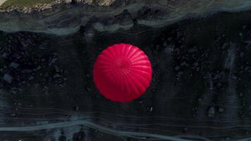 aéreo topo Visão do uma voar do uma vermelho quente ar balão sobre a falésias dentro a interior. tomada. vôo acima a rochoso montanha declive, verde Prado, e uma limitar caminho. video