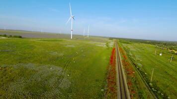 oben Aussicht von schön Eisenbahn auf Hintergrund von Grün Feld. Schuss. Wind Bauernhof in der Nähe von schön Eisenbahn im Grün Feld. malerisch Eisenbahn mit rot Blumen im Grün Feld mit Windmühlen video