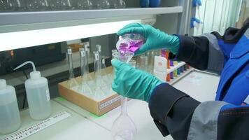 chemie concept. klem. een Mens in handschoenen wie tests een roze vloeistof voor een experiment. video