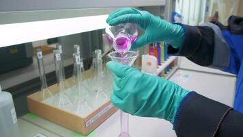 química concepto. acortar. un hombre en guantes quien pruebas un rosado líquido para un experimento. video
