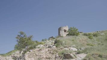 Ancient ruined castle on the top of the hill on blue clear sky background. Action. Broken abandoned stone building on green field. video