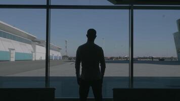 Back view of a confident successful male silhouette in front of a large window. HDR. Thoughtful businessman watching the summer blue sky and a parking space. video