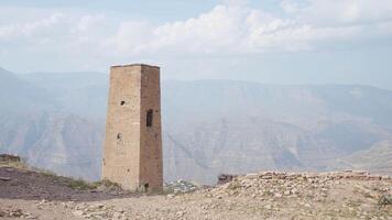 Ruined old stone tower on mountains background. Action. Ancient abandoned tower in mountainous region under the bright sun. video