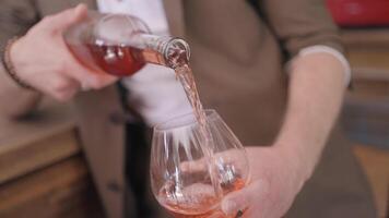 proche en haut de une homme dans beige costume verser Rose du vin dans une transparent verre. action. Masculin sommelier verser fruit du vin à une bar. video