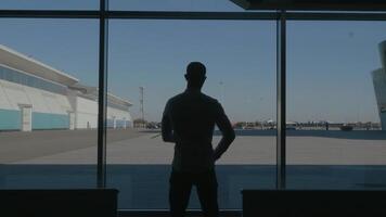 silhouet van een zakenman terug met uitzicht de parkeren ruimte achter de venster. hdr. achterzijde visie van een jong Mens staand in voorkant van panoramisch venster binnen de bedrijf centrum. video