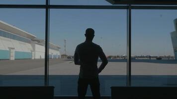 Silhouette of a businessman back overlooking the parking space behind the window. HDR. Rear view of a young man standing in front of panoramic window inside the business center. video