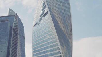 bodem visie van een gedraaid wolkenkrabber Aan blauw bewolkt lucht achtergrond. actie. glas facade hoog gebouwen in de bedrijf stad centrum. video