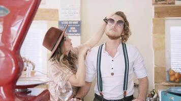 Portrait of a man with curly long hair in white shirt and blue suspenders. Action. Stylist woman preparing male model before the photo session. video