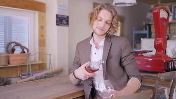 A handsome man with curly blond hair in beige suit pouring rose wine into a transparent glass. Action. Male sommelier pouring fruit wine at a bar. video