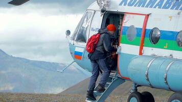 instappen een helikopter. klem. mannen invoeren een helikopter dat staat in de Woud tegen de achtergrond van een mistig lucht en reusachtig bergen. video