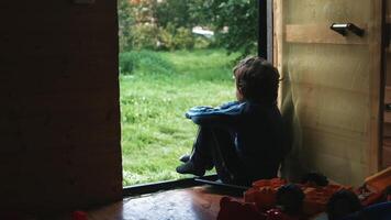 un sentado chico. creativo. un pequeño chico quien mira a el verde calle siguiente a su juguetes en el habitación video