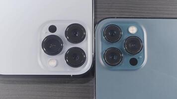 Saint Petersburg - Russia, 10.11.2021. close up of three cameras of new iPhone 13 pro max. Action. Stylish design and professional cameras of new blue and silver smartphones lying on wooden surface. video