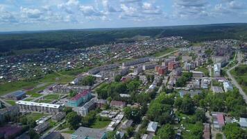 se från en helikopter. klämma. en små grön sommar stad med parker och hus för människor , en stor skog och kullar med grön fält är synlig från Bakom video