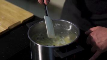 dichtbij omhoog van voorbereidingen treffen soep, bouillon met aardappel en zwart peper granen. kunst. chef handen roeren soep met een keuken spatel. video