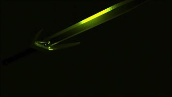 A medieval sword of green color flying against black backdrop. Design. Game of light and shadow, concept of war or battle, sharp weapon in the dark. video