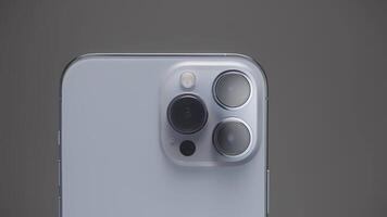 Saint Petersburg - Russia, 10.11.2021. close up of three cameras of new iPhone 13 pro max. Action. Stylish design and professional cameras of new silver smartphone against grey wall. video