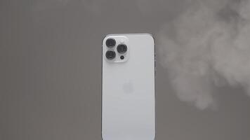 New York - USA, 10.11.2021. close up of a new Iphone 13 pro max with three cameras. Action. Steam spreading around a new silver smartphone rotating slowly isolated on a beige wall background. video