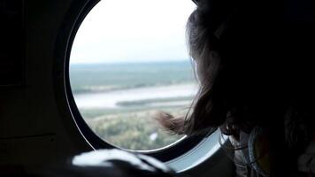 ver desde el avión ventana. acortar. un niña con revoloteando pelo mirando a el paisajes de el tierra desde el altura de un aeronave tomando apagado video