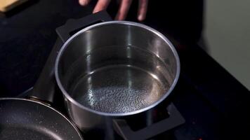 Close up of preparing soup, boiling water in a stainless pot. Art. Top view of transparent water getting hotter inside a pot on a black stove surface background. video