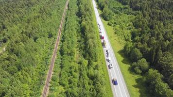 A wonderful green road from a helicopter . Clip. A long paved road with cars and a huge green summer forest around. video