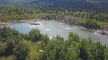 un hermosa azul lago. ver desde el zumbido acortar. un pequeño lago siguiente a cuales son verde soleado árboles, detrás el bosque y montañas y claro cielo. video