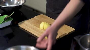 een Mens snijdend een geschild aardappel Aan een houten bord. kunst. dichtbij omhoog van mannetje chef voorbereidingen treffen een schotel en gebruik makend van een staal mes voor snijdend groenten. video