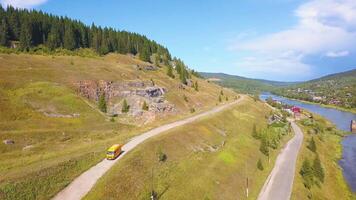 Wonderful bird's-eye view. Clip. A green hilly mountain on which there are roads with cars and a bus, on top of which there is a forest and a river below, on the right side you can see the other bank video