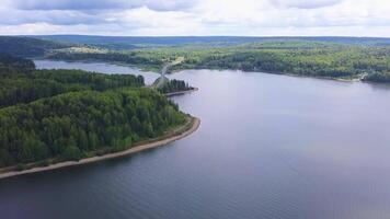 de se från de drönare.a enorm sjö med en bro. klämma. en enorm damm runt om med en stor grön skog och en ljus molnig himmel . video