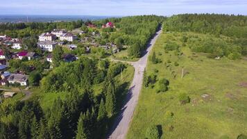 Beautiful view from the helicopter . Clip. A beautiful green summer road near the city, with small residential buildings and a beautiful landscape of forests, mountains and misty fields. video