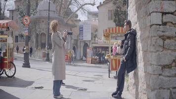 kvinna fotografier ung man i gammal europeisk stad. handling. sida se av kvinna fotografering man med kamera. skytte man på professionell kamera i gammal stad video