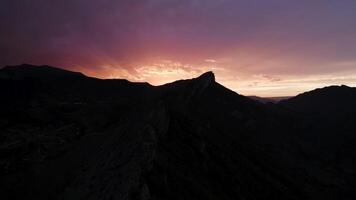Antenne Aussicht von Berg Angebot im Vorderseite von atemberaubend Sonnenaufgang. Aktion. bunt Himmel kontrastieren mit schwarz Felsen Silhouette. video