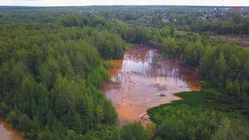 vervuild rivier. klem. een vuil rood rivier- met een mooi Woud in de omgeving van en achter de huizen. video