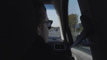 bak- se av en ung man i svart solglasögon ser genom de sida bil fönster. hdr. man njuter sommar rida inuti de fordon. video