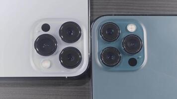 Saint Petersburg - Russia, 10.11.2021. close up of three cameras of new iPhone 13 pro max. Action. Stylish design and professional cameras of new blue and silver smartphones lying on wooden surface. video
